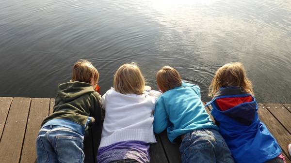 Vier Kinder liegen auf Steg und beobachten das Wasser