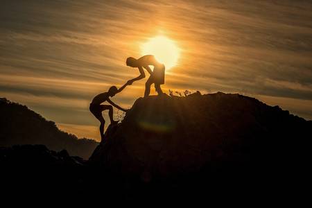 Junge hilft anderem Junge beim Erklimmen eines Berges im Gegenlicht der Sonne
