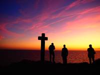 Menschen stehen bei Kreuz vor Sonnenuntergang